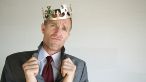 A cocky-looking sales professional wearing a crown to suggest that he thinks he is king pin as a result of his charisma.