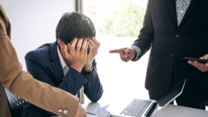 A stressed-looking sales executive having coaching dictated to them by two sales managers.