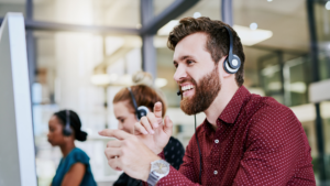 A helpful sales executive sitting at his desk, wearing a headset, looking pleased as he assists a customer over the phone.